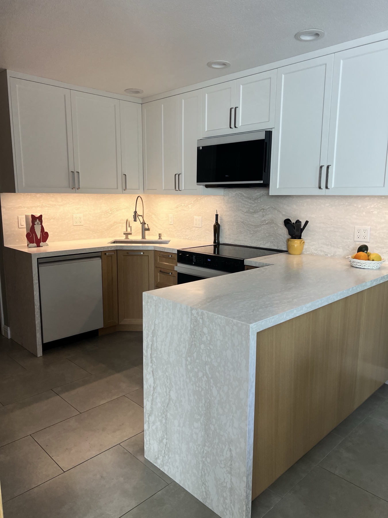 Upper cabinet doors with vertical bar pulls above the lit backsplash