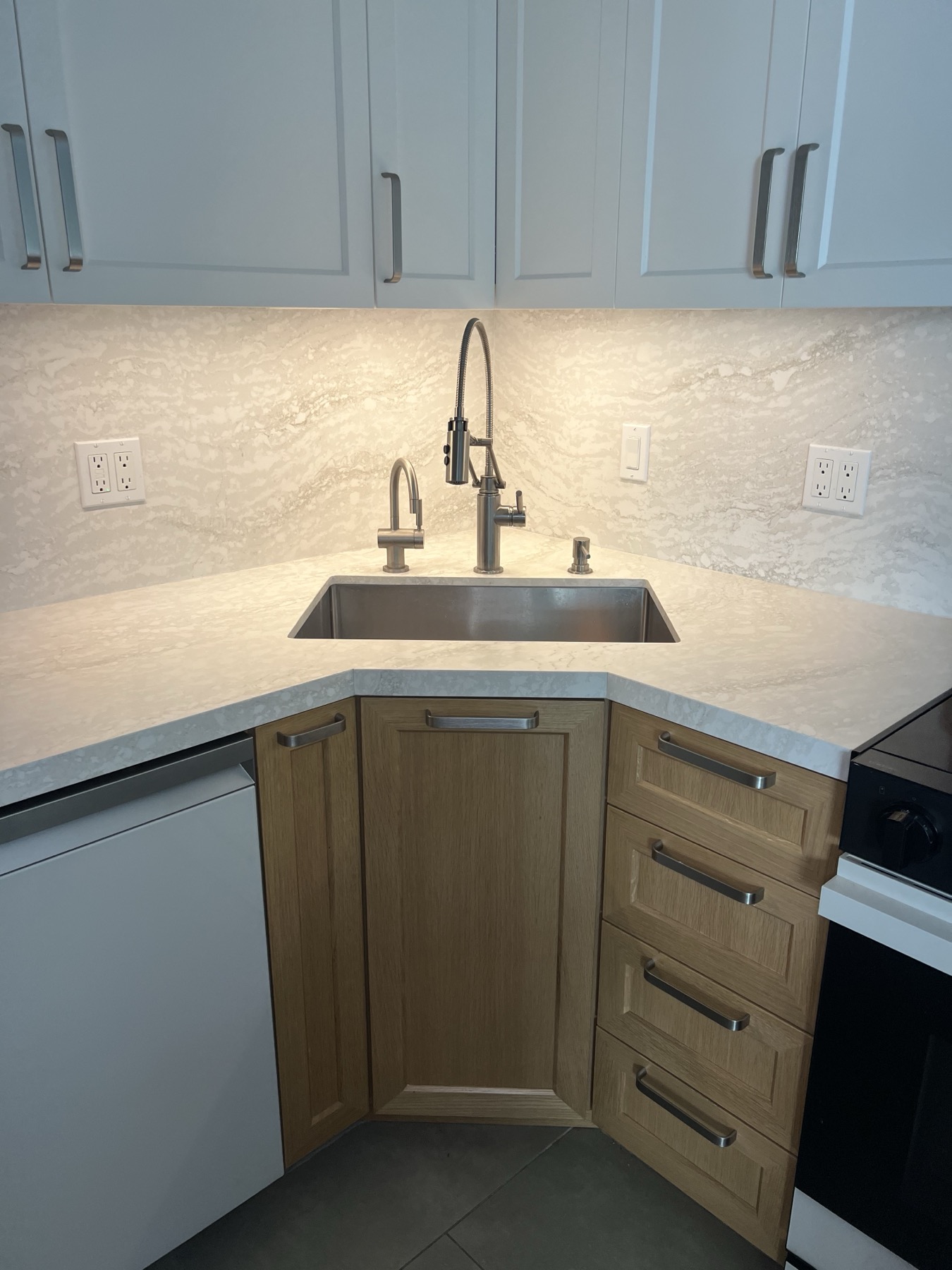 Stainless sink set across the corner over an angled warm-wood base cabinet